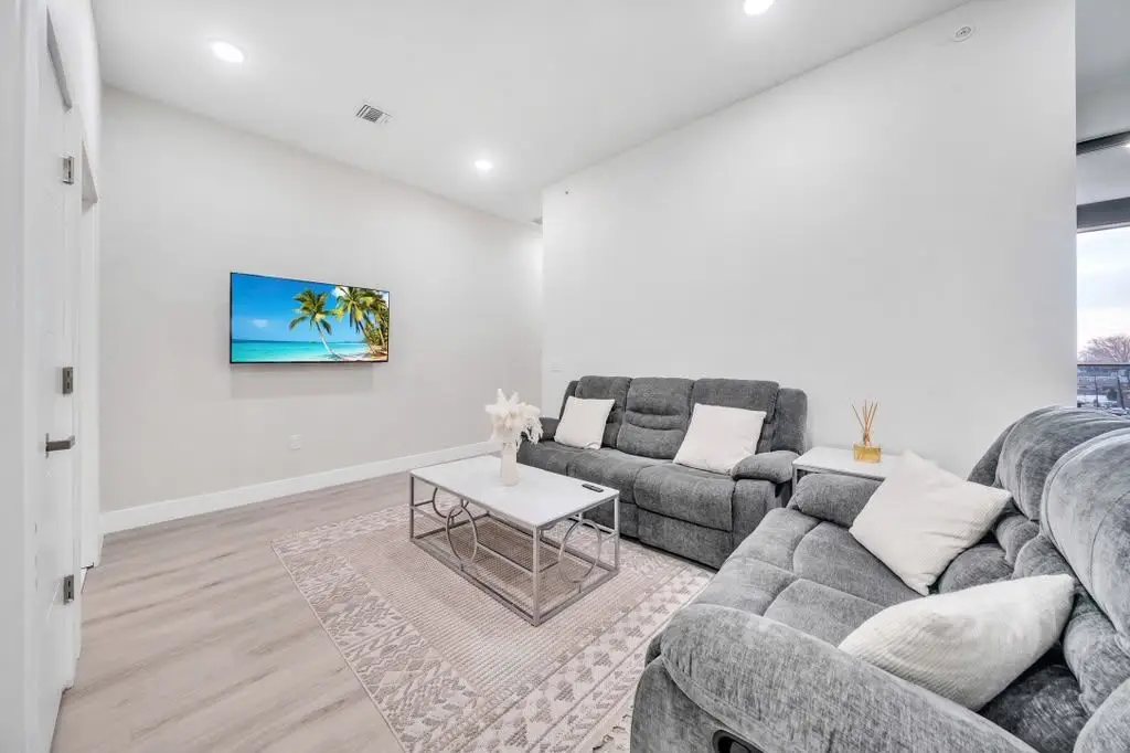 Living room with grey reclining sofa, glass coffee table and wall-mounted TV, Residence 106