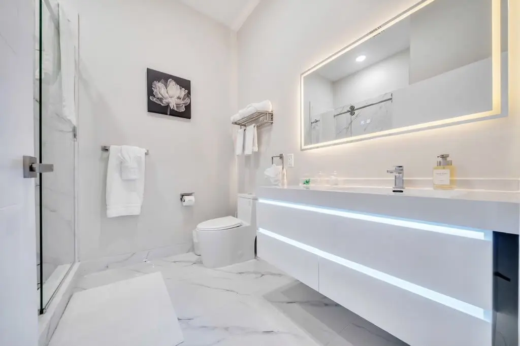 Bathroom with floating white vanity, lit mirror and glass shower, Residence 106