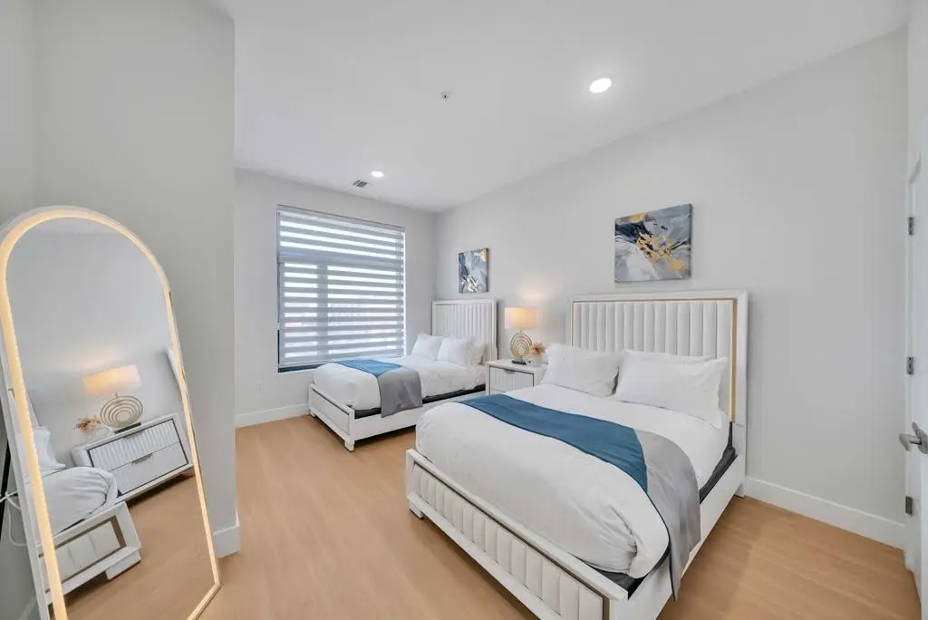 Bedroom with two beds, an arched floor mirror and a window with zebra blinds, Residence 304