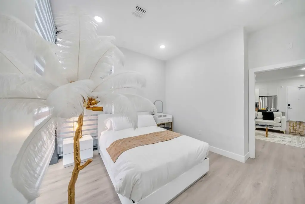 Bedroom with white bed, tan throw and a white feather palm decoration, Residence 407
