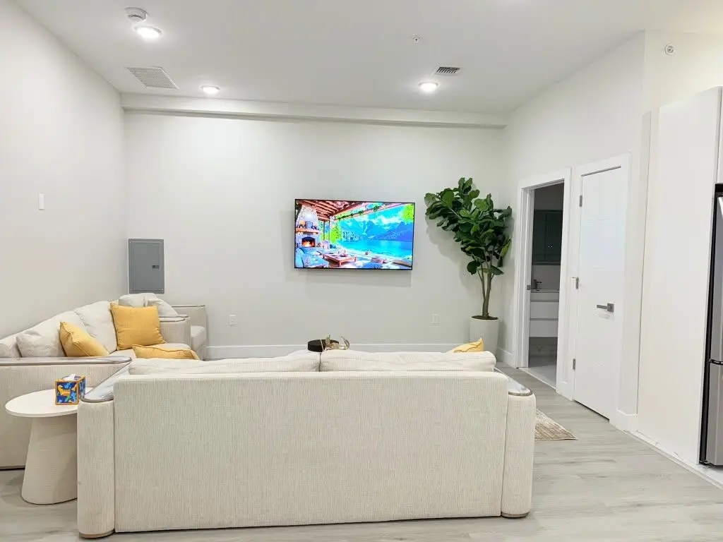 Living room with cream sofa with yellow cushions, wall-mounted TV and a potted tree