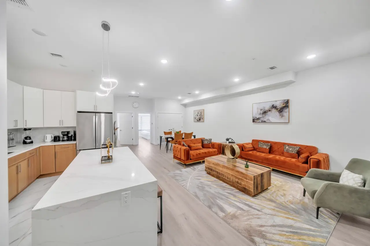 Open-plan living area with orange sofas, wooden coffee table and kitchen island, Residence 414
