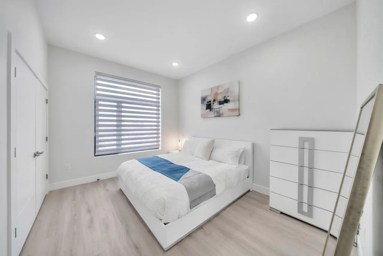 Bedroom with white bed, blue throw, tall white dresser and a ladder at the edge of the frame, Residence 414