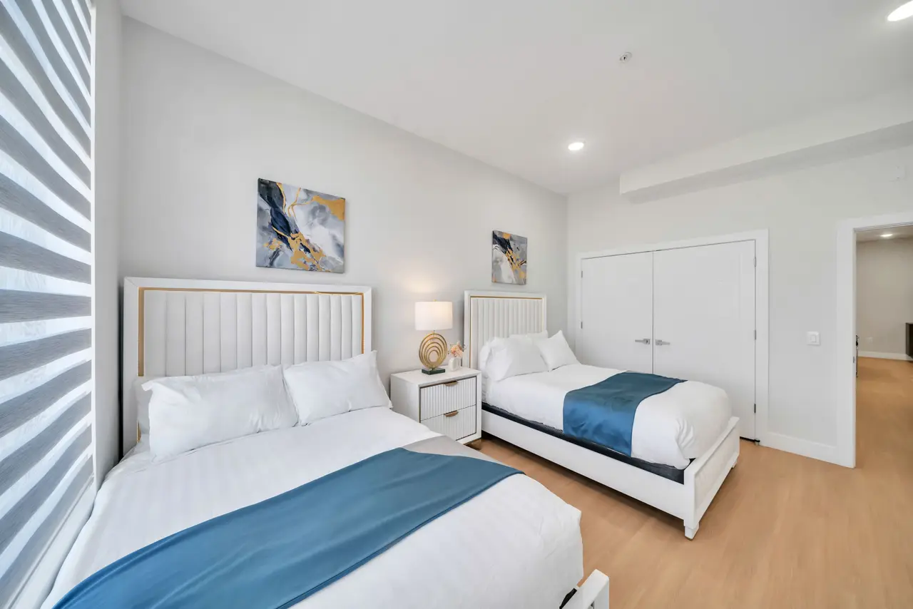 Bedroom with a large bed and a second bed, white tufted headboards and blue throws, Residence 304